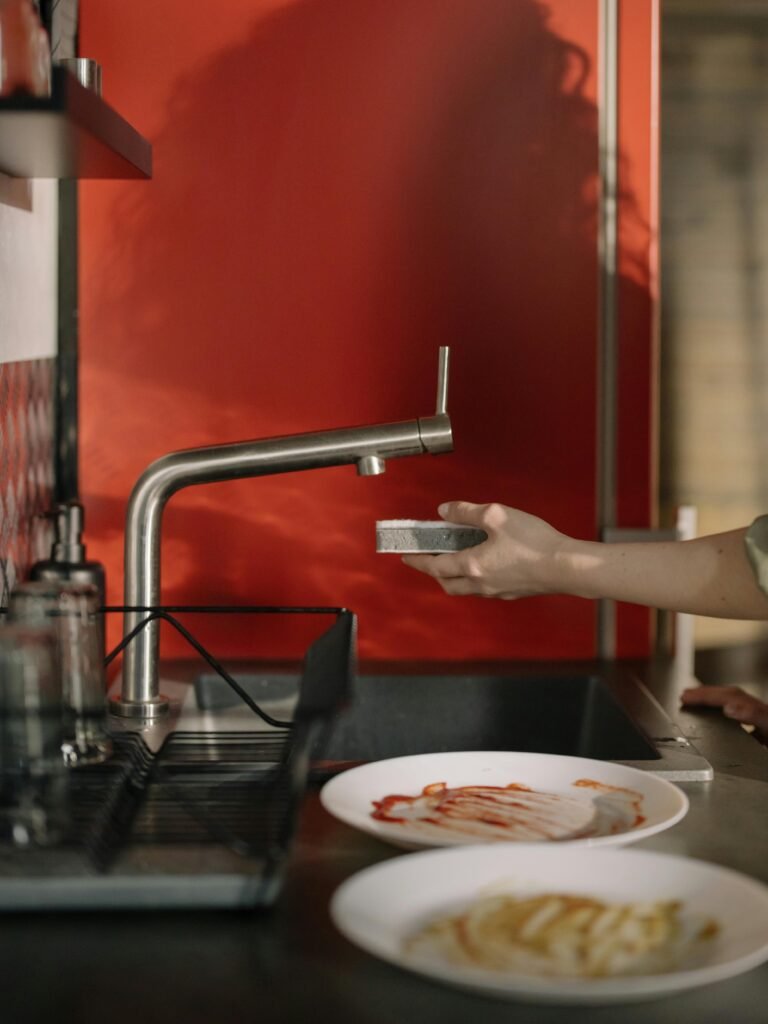 Close-up of a hand washing dishes in a modern kitchen with a red backdrop.